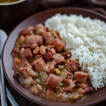 red beans and sausage next to rice on brown plate with cornbread on the side