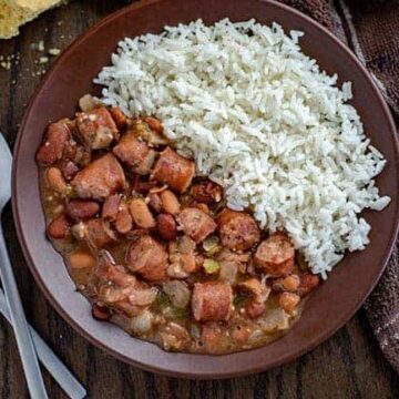 red beans and sausage next to rice on brown plate with cornbread on the side