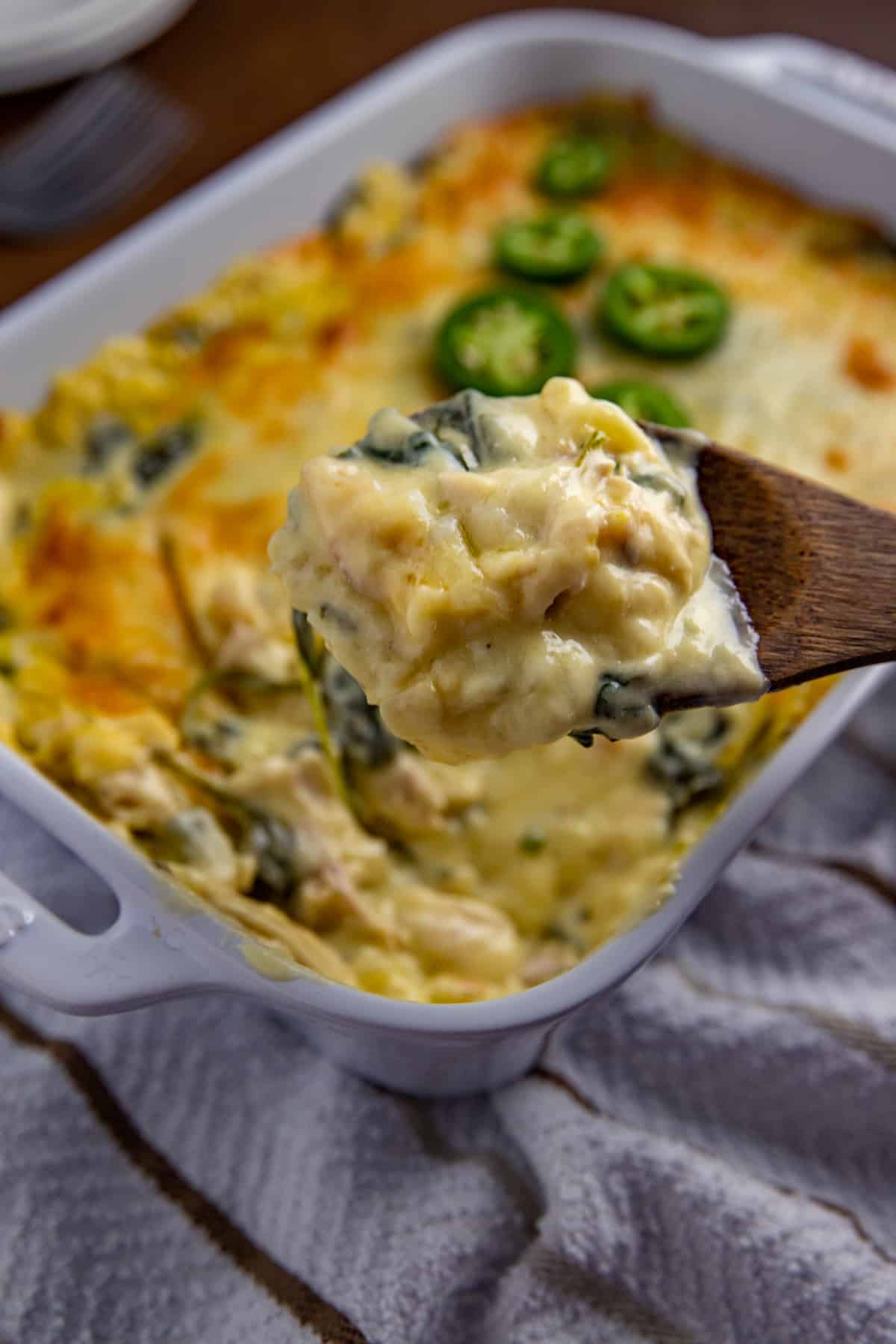 baked keto mexican casserole in oblong white dish with wooden spoon scooping out a serving.