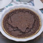Whole Chocolate Chess Pie in white pie plate with silver pie server on the side and blue napkin