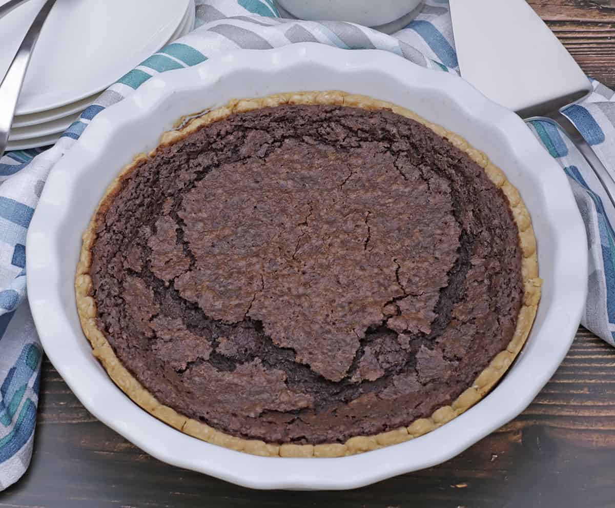 Whole Chocolate Chess Pie in white pie plate with silver pie server on the side and blue napkin