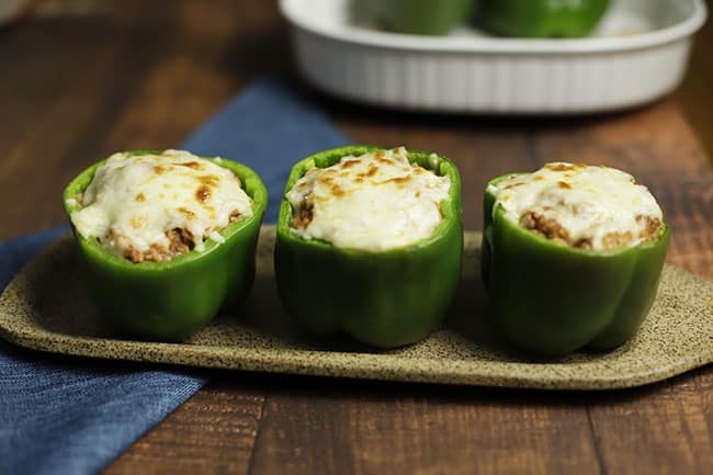 three baked stuffed bell peppers on brown serving platter with blue napkin