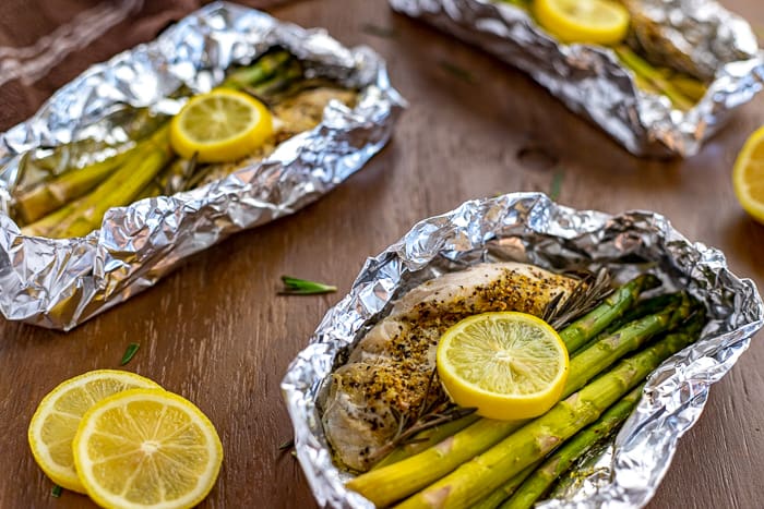 Lemon Pepper Chicken with rosemary and asparagus inside foil packet with lemon slices on top