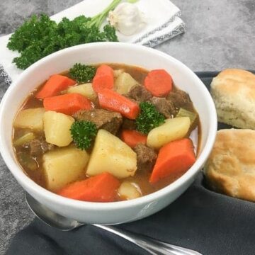 Beef and Vegetable Stew in White Bowl with two biscuits on the side