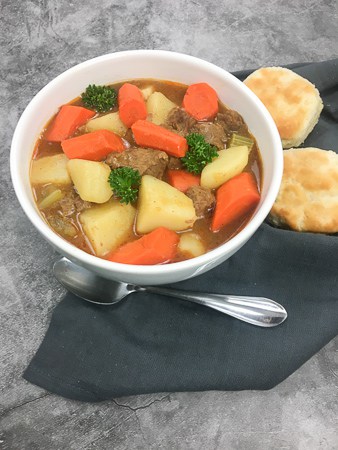 beef and vegetable stew in white bowl with two biscuits on the side
