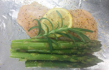 raw chicken breast with asparagus spears and lemon slice and rosemary sprig inside a piece of foil