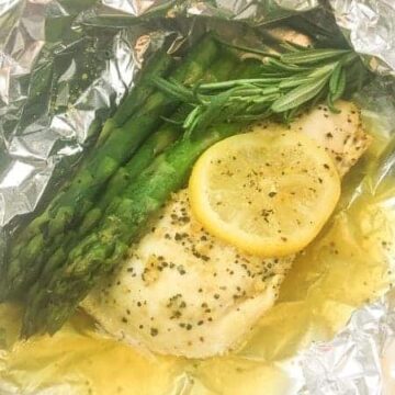 lemon pepper chicken and asparagus with rosemary inside a foil packet showing juices