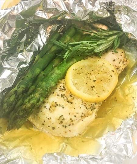 lemon pepper chicken and asparagus with rosemary inside a foil packet showing juices