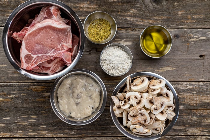 Overhead view of pork chops and ingredients in silver bowls on a table. 