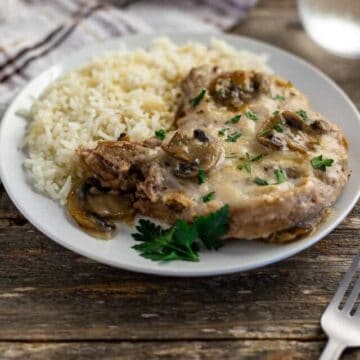 cooked pork chop covered with mushroom gravy on white plate with rice on the side