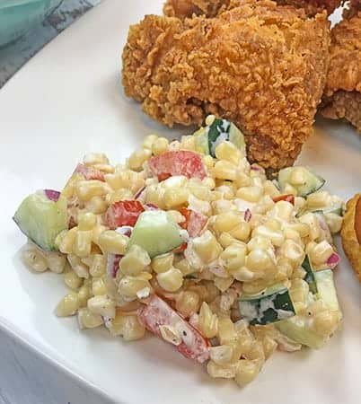 creamy corn salad on white plate next to fried chicken
