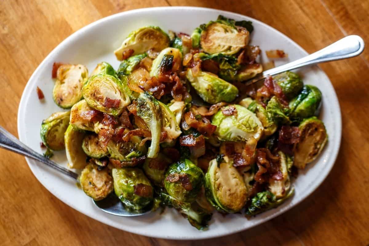 roasted brussels sprouts with bacon in white bowl with two forks