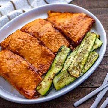 Four BBQ Grilled Salmon Fillets on white platter with grilled zucchini slices on the side