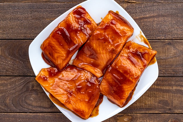 BBQ marinade on 4 uncooked salmon fillets on white square plate