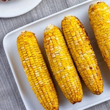 five ears of grilled corn on white rectangle platter.