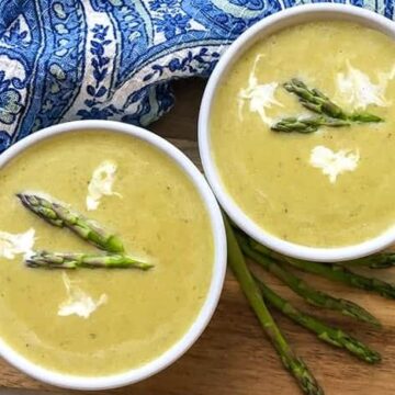 two white bowls filled with creamy asparagus soup and asparagus spears as garnish
