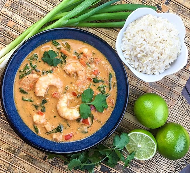 soup in blue bowl with cup of white rice on the side.  Fresh green onions and limes in the background.