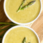 two white bowls filled with creamy asparagus soup and asparagus spears as garnish