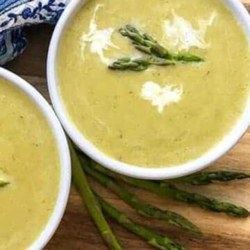 two white bowls filled with creamy asparagus soup and asparagus spears as garnish