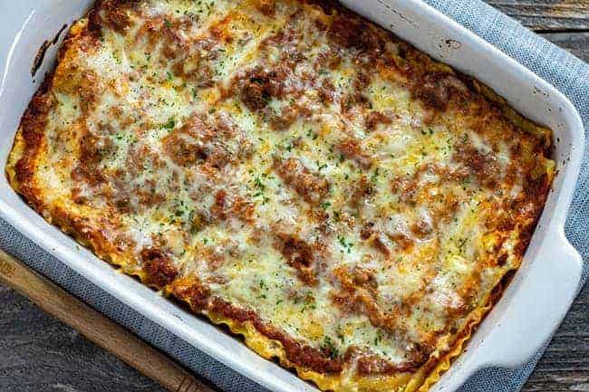 baked meat lasagna in a white casserole dish on a wooden table