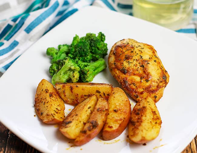 baked sliced potato wedges and chicken breast on white plate with broccoli on the side