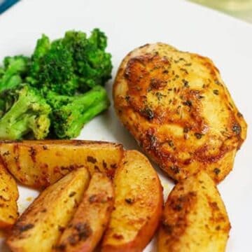 baked sliced potato wedges and chicken breast on white plate with broccoli on the side