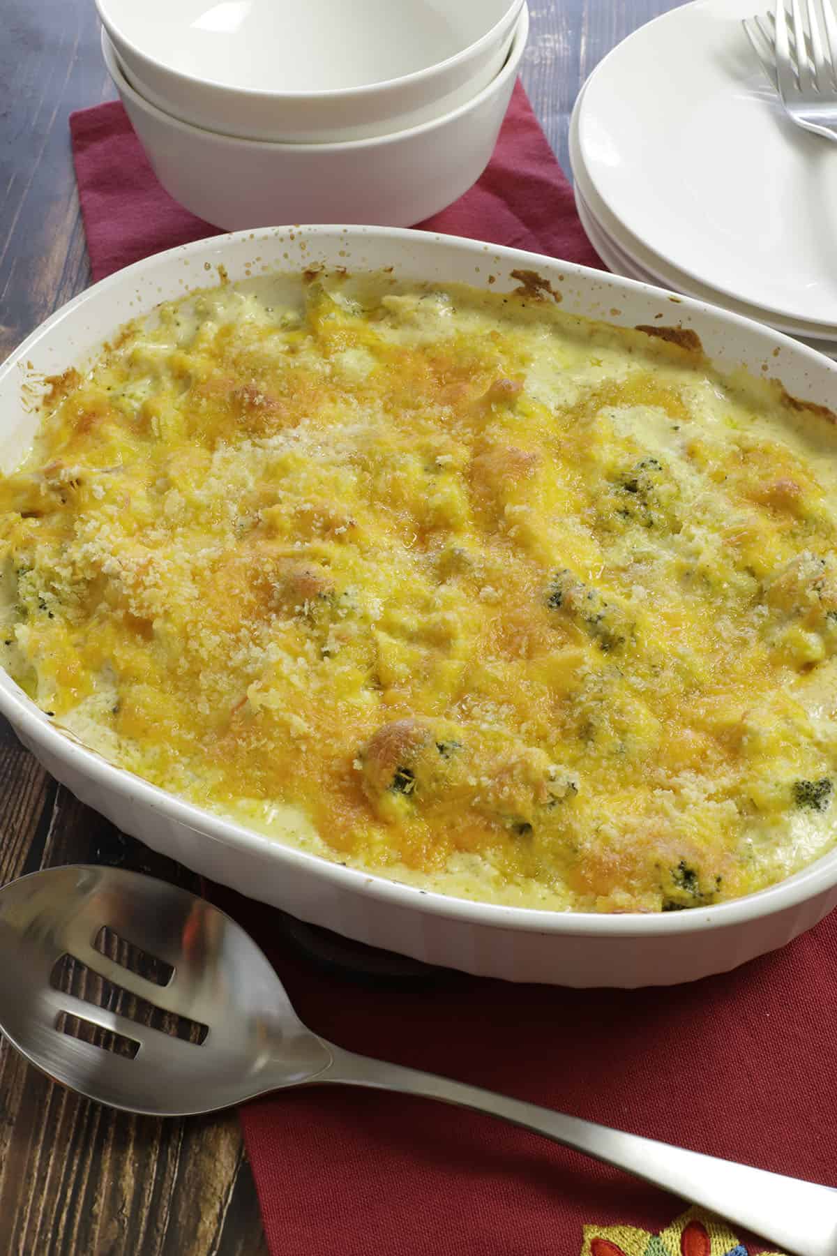 Cheesy baked casserole in oval white dish with silver spoon and red napkin on the side.