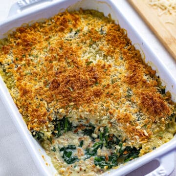 baked casserole in white casserole dish with scoop of spinach parmesan taken out