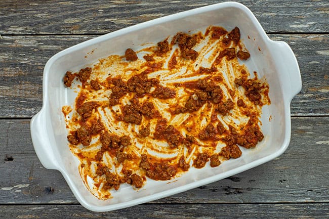 thin layer of red meat sauce in white casserole dish