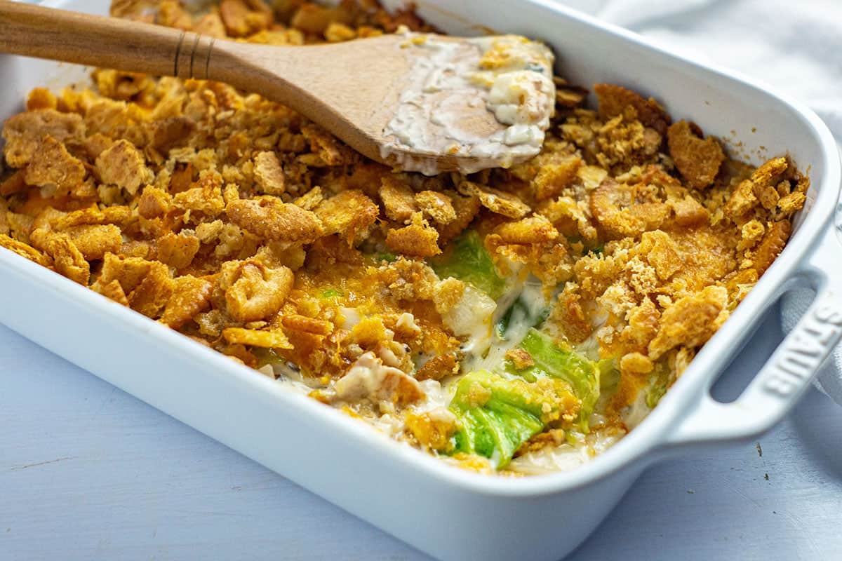 baked casserole in a white oblong dish with one serving removed and wooden spoon sitting on top of casserole