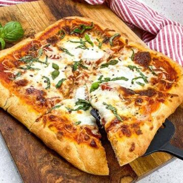 baked pizza on wooden cutting board with slice on spatula