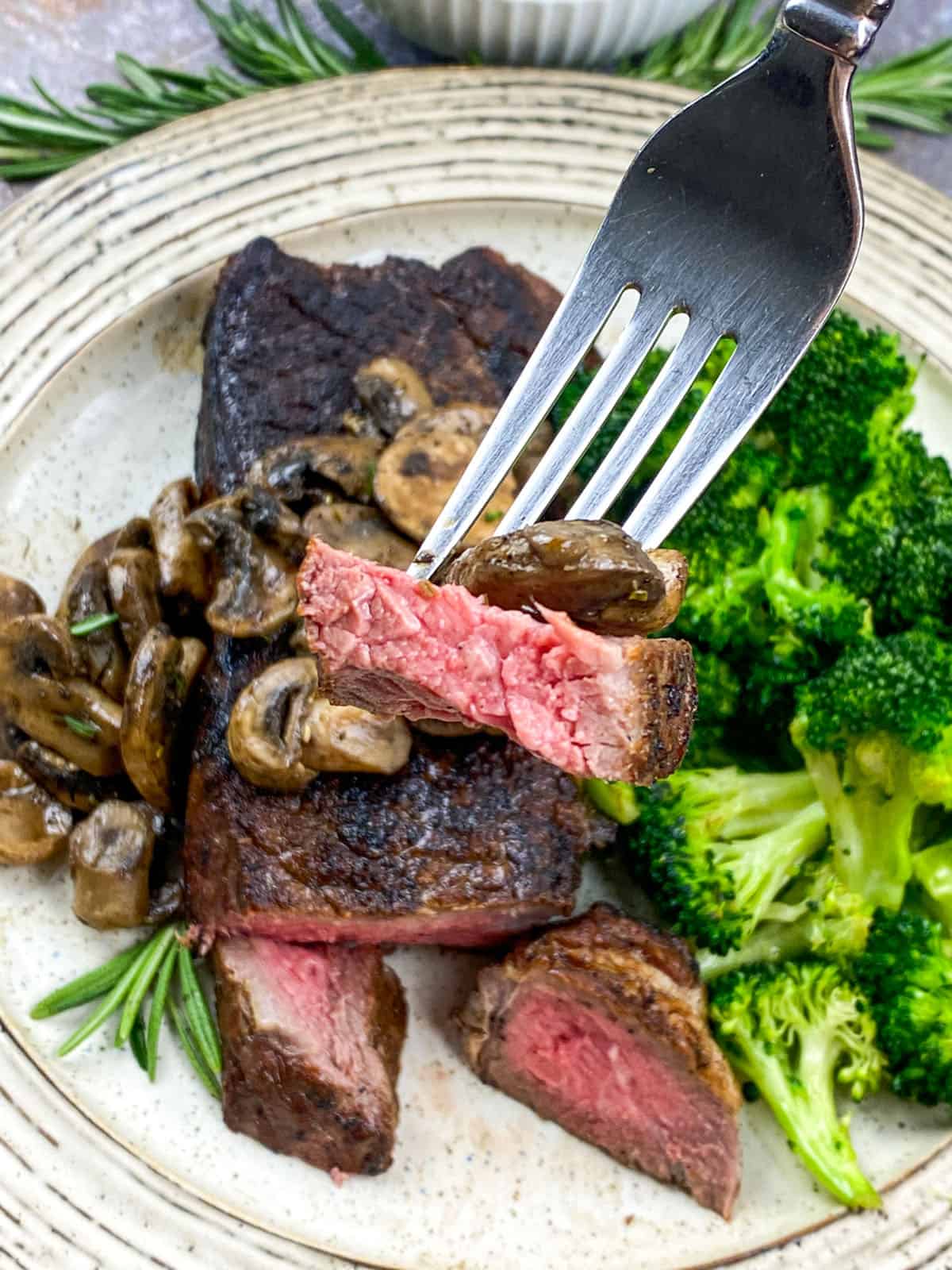 Medium rare strip steak with mushrooms and broccoli on white plate