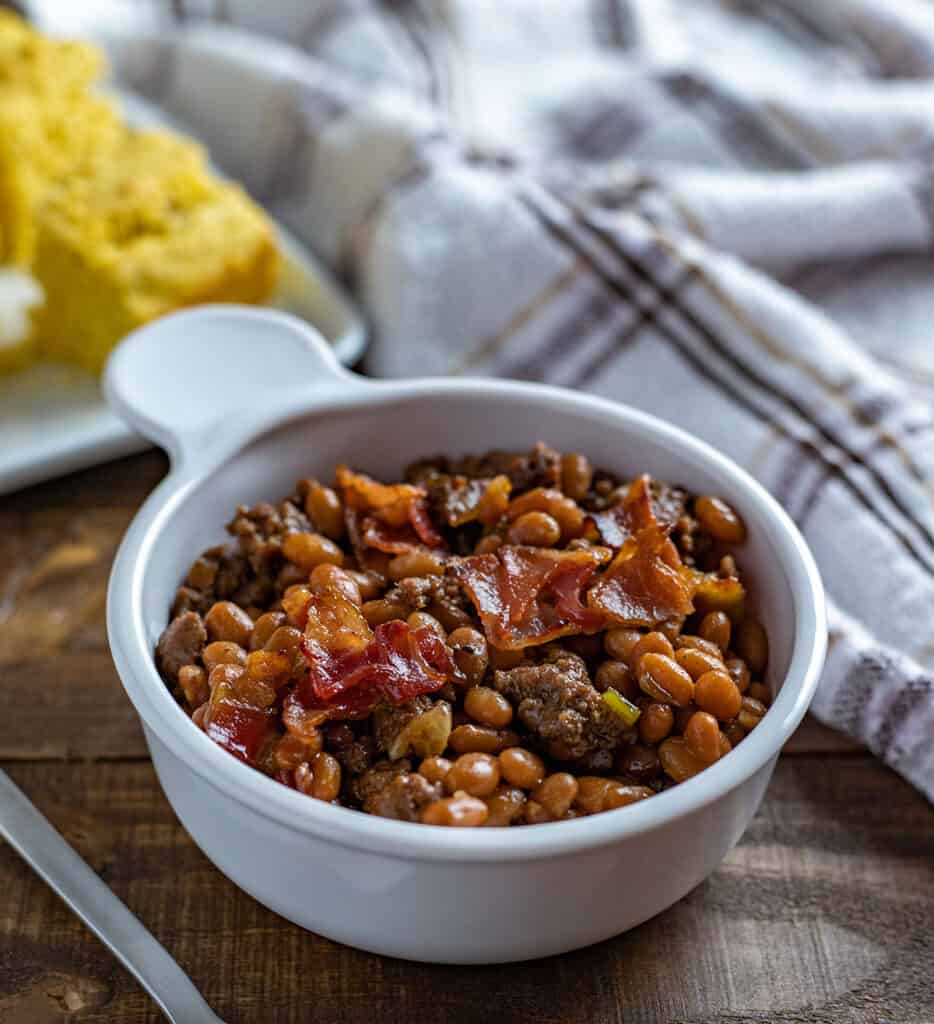 white bowl with baked beans.  Slices of cornbread in background