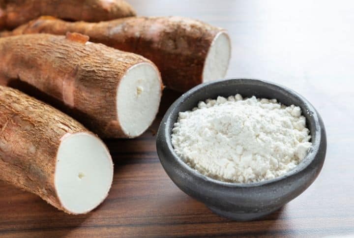  farine de manioc dans un bol à côté du manioc entier