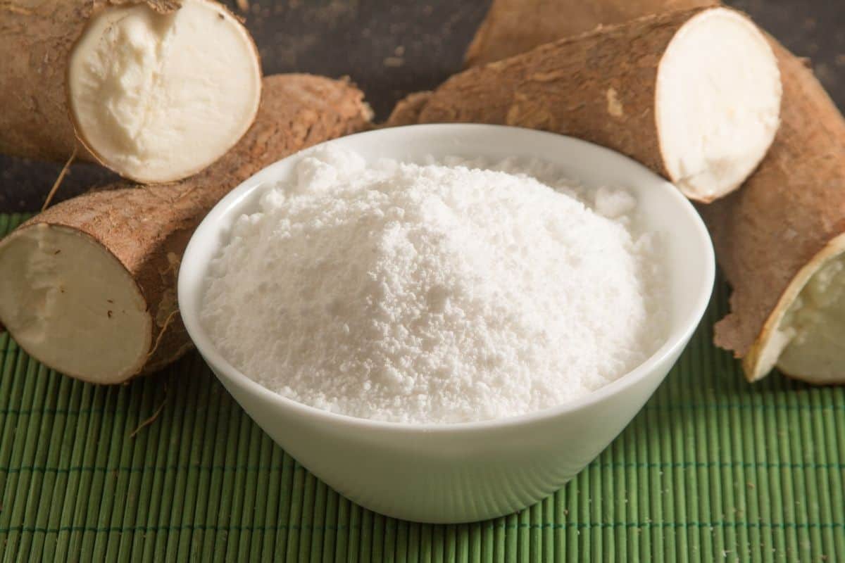 cassava flour in white bowl next to whole cassava