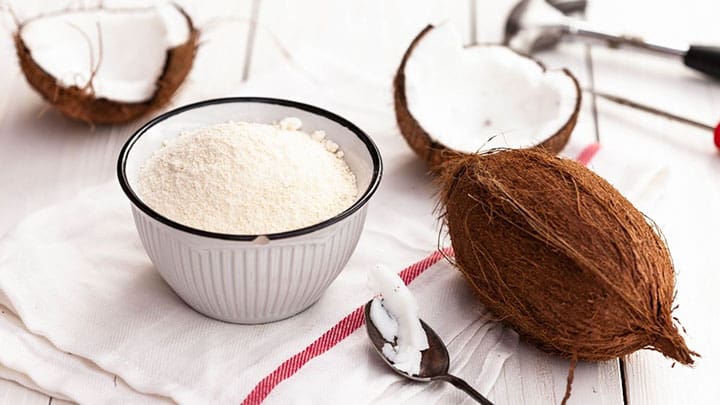  farine de noix de coco dans un bol avec de la noix de coco entière à côté