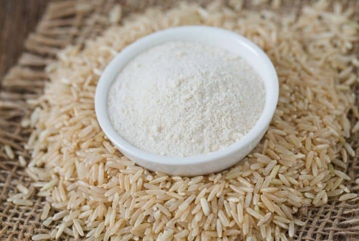  farine de riz dans un bol avec du riz entier éparpillé autour du bol