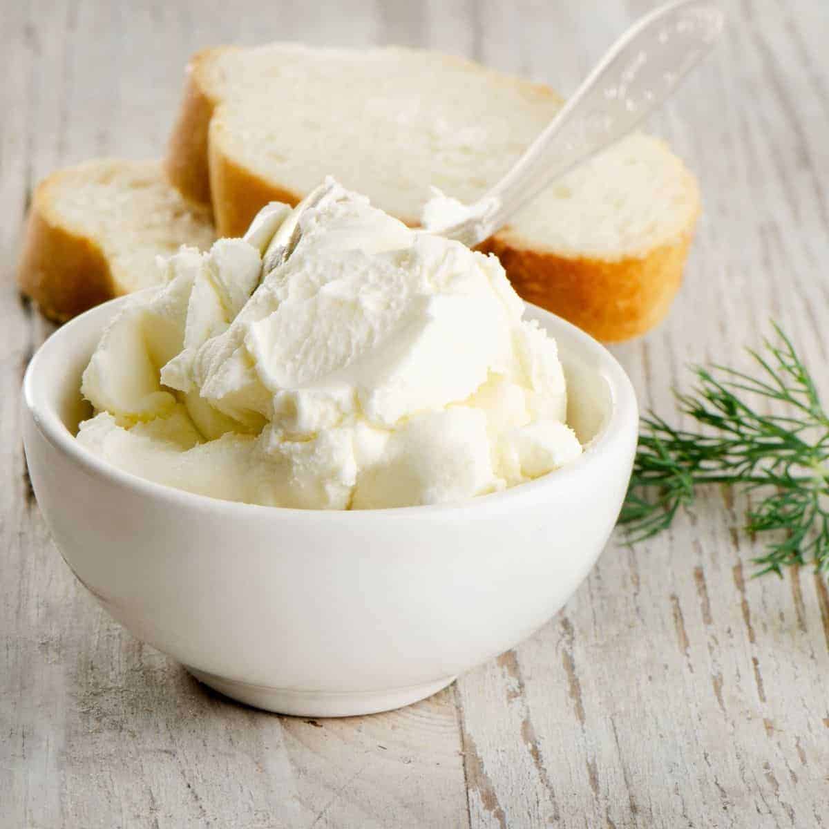 cream cheese in white bowl with clear spoon and 3 slices of french bread in background