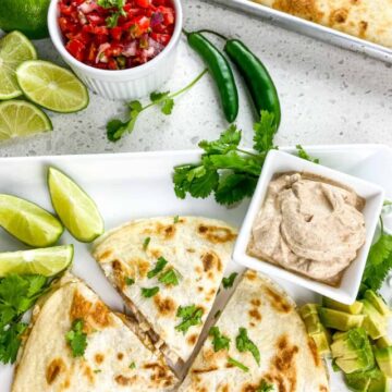 cooked quesadillas cut into thirds on white rectangular plate with lime wedges and seasoned sour cream and pico de gallo on side