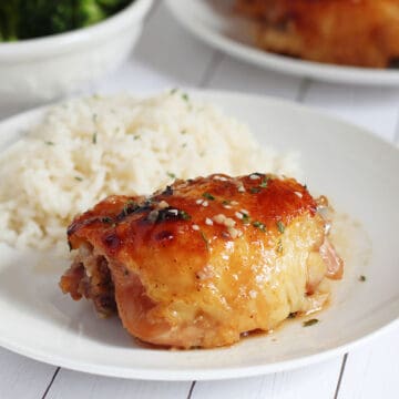 baked chicken thigh and white steamed rice on white place with broccoli in background