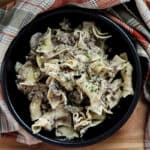 cooked stroganoff in black bowl with red plaid napkin