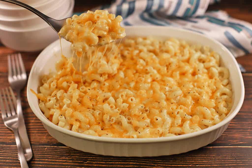 baked cheese macaroni in white oblong casserole dish with silver spoon scooping