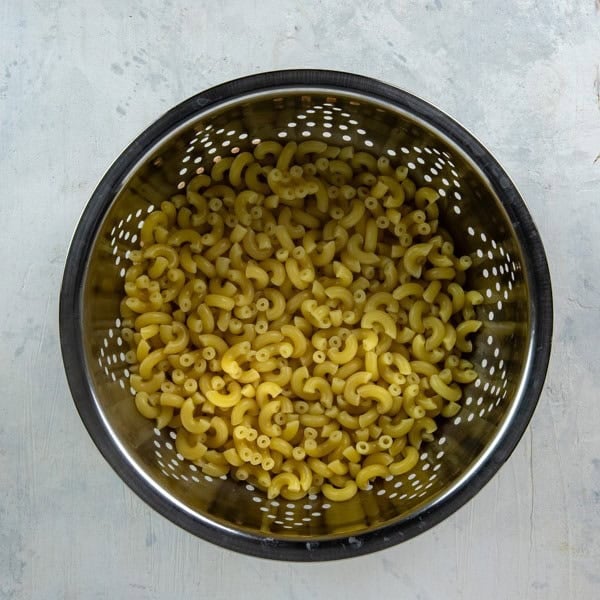 Cooked and drained macaroni in a pasta strainer.