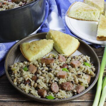 cooked hoppin john on brown plate with 2 slices of cornbread and green onions on the side.