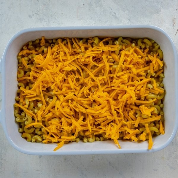 Macaroni mixture poured into a white casserole dish with more cheese sprinkled on top.