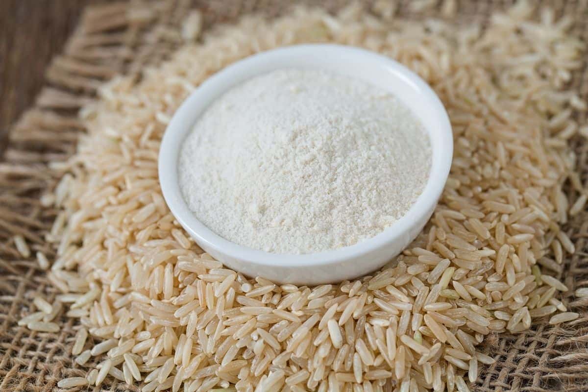 rice flour in white bowl sitting on top of uncooked grains of rice