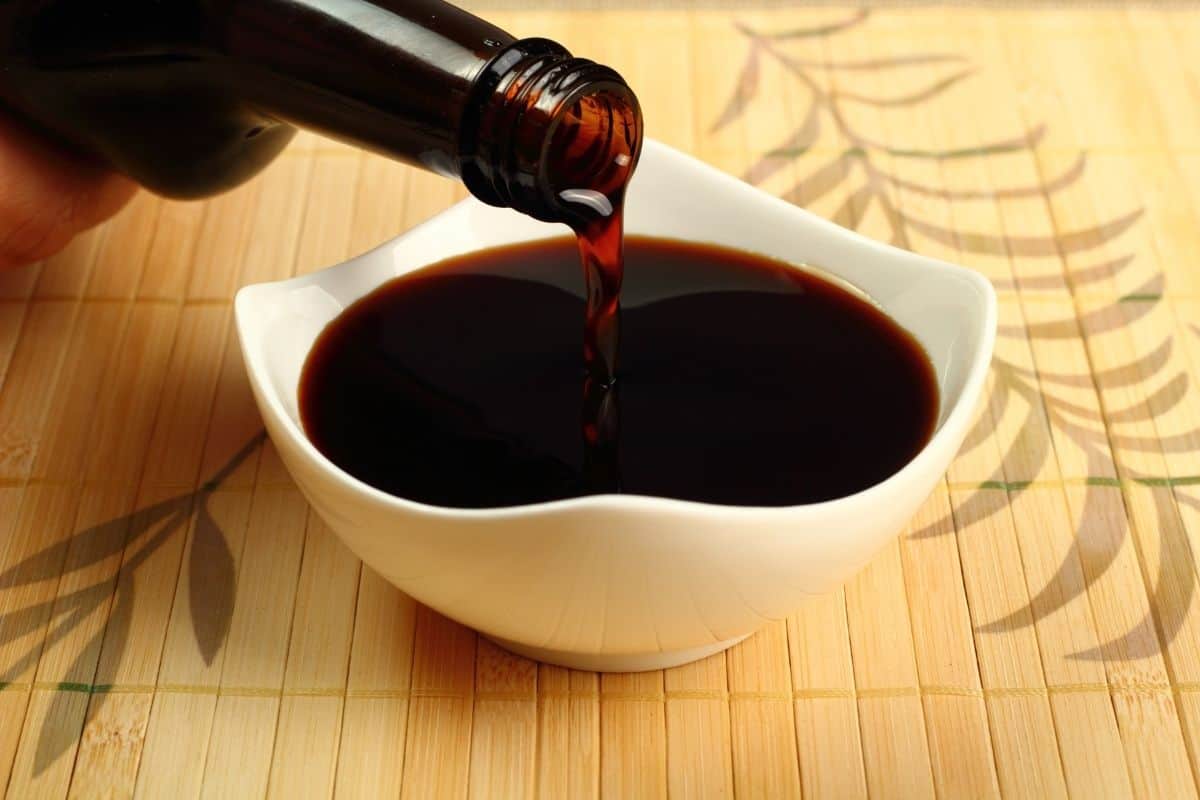 bottle of soy sauce pouring into white bowl