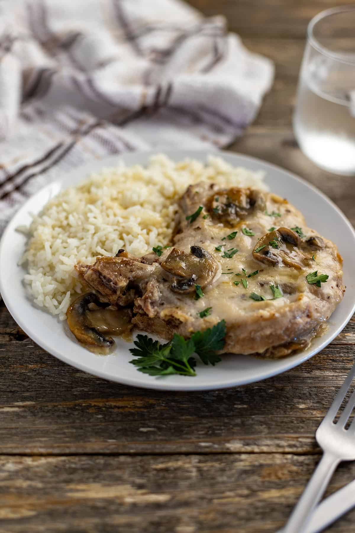 cooked pork chop topped with mushroom gravy with a side of rice on white plate