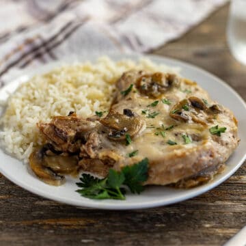 cooked pork chop topped with mushroom gravy with a side of rice on white plate