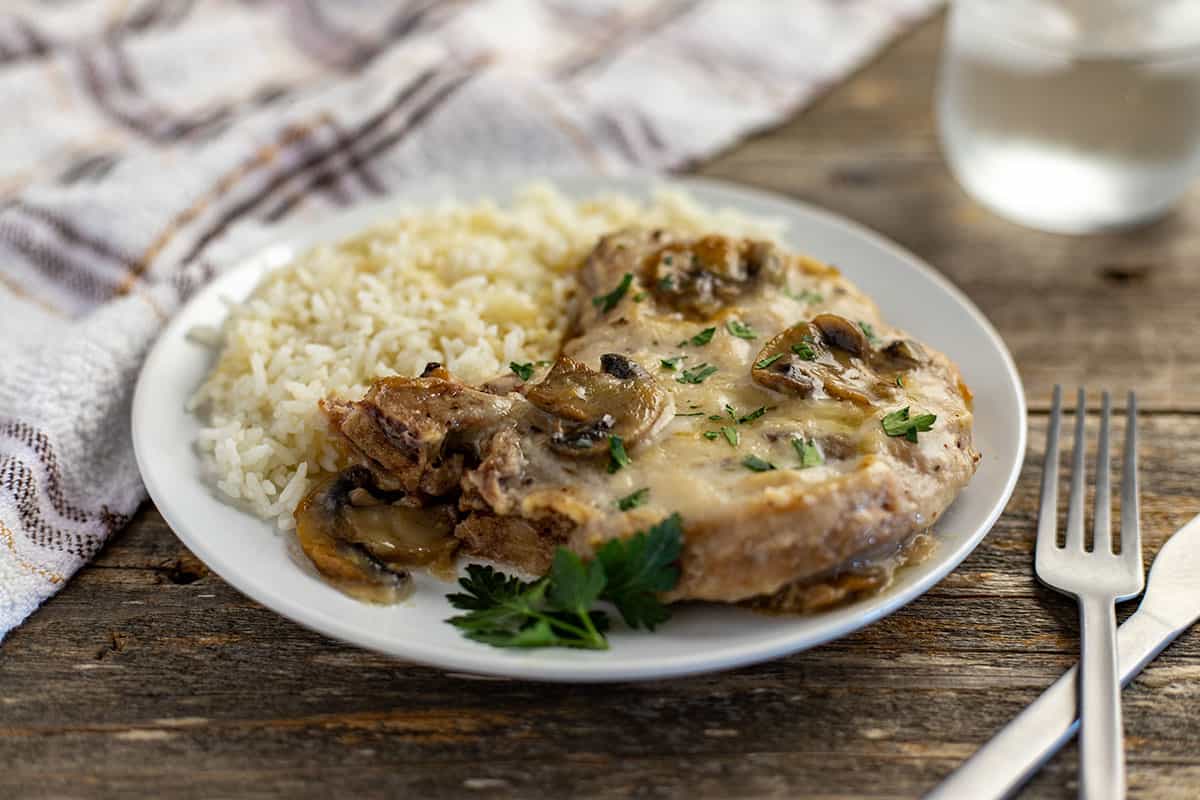 cooked pork chop topped with mushroom gravy with a side of rice on white plate